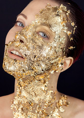 Closeup portrait of beautiful young woman with golden foil on face. Creative makeup.