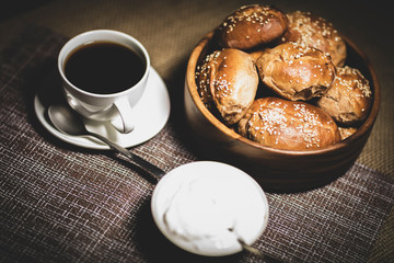 Pies in a wooden plate, a cup with a hot drink and a plate with sour cream stand on a table covered with a linen tablecloth.
