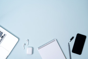 Flat lay of composition with laptop, phone, wireless headphones,  notepad on light blue background with copy space for text.
