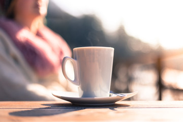 Cup of coffee on the table of a café, outdoors in the sunny afternoon. Woman in the blurry background.