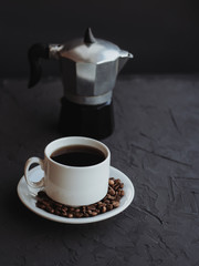 White cup of coffee and coffee beans on a dark background