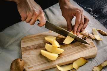 Chef's hand cutting fresh and delicious potatoes for cooking on a table. Healthy food.