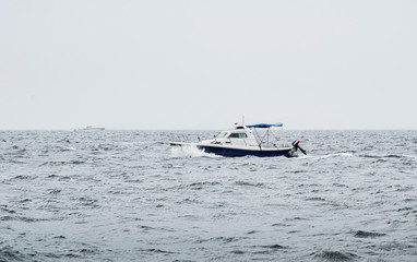 Obraz premium A motorboat floating on the heavy sea with waves in bad weather conditions with other luxury yacht on background. Boat on the ocean (overcast day) after the storm - image