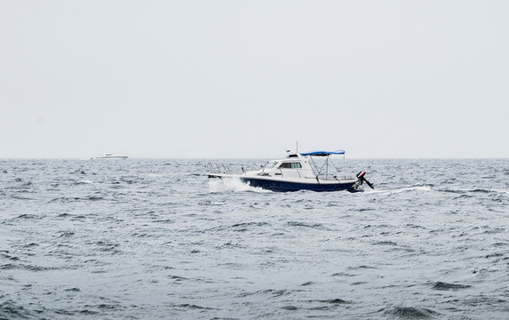A motorboat floating on the heavy sea with waves in bad weather conditions with other luxury yacht on background.   Boat on the ocean (overcast day) after the storm - image