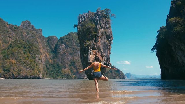Traveler woman doing yoga fitness exercise on sea beach in front of famous tourist destination landmark James Bond island in Thailand, Asia
