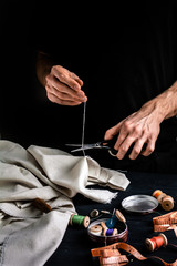 Tailor cutting a thread with scissors, close up, black background