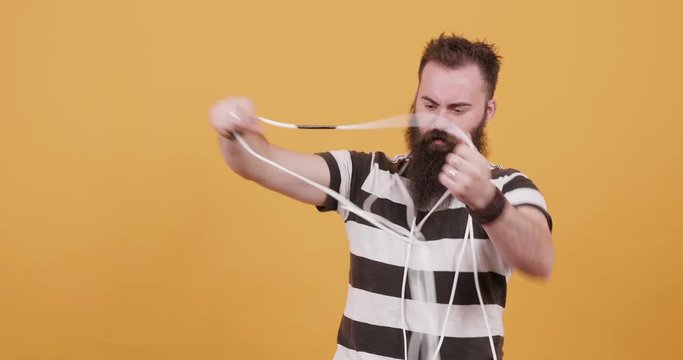 Funny bearded man tries to untagle the electric cables. Young hipster man covered in cables trying to solve the problem in a funny way. Wire problem.