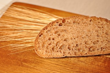 One cereal brown slice, with dried wheat decoration on wooden table background. Front view, copy...