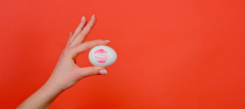 Print of red lips on white egg. Red lip imprint on easter egg on red background.