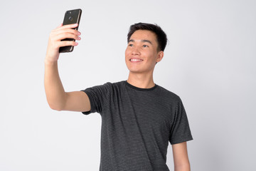 Portrait of young happy Asian man taking selfie