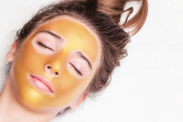 Beautiful girl with a cosmetic mask on the face of golden color. Close-up. Free space. Woman gold mask. Beautiful model removing golden facial skin cosmetic. Beauty skincare .