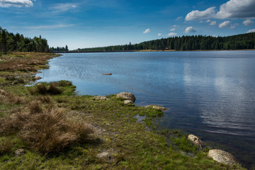 Daily landscape at dam in the mountain. Stones in the foreground. Blue sky with clouds is mirroring into water surface.