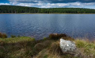 Daily landscape at dam in the mountain. Stone in the foreground. Blue sky with clouds is mirroring into water surface.