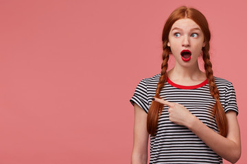 Shocked worried teen girl with two red haired braids red lipstick open mouth in panic pointing...