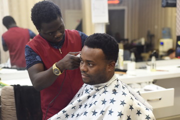 Black man in the african barbershop. Cute black man makes a haircut in the African salon. Hair style. Haircut by machine for adults. 