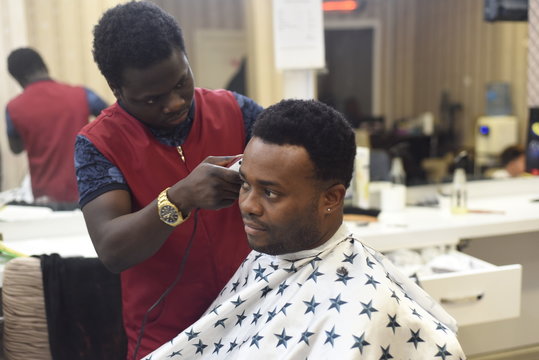 Black man in the african barbershop. Cute black man makes a haircut in the African salon. Hair style. Haircut by machine for adults. 