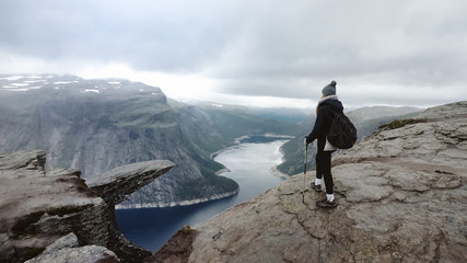  Adventurous girl with trekking poles walk mountain trail. Rocky part of path with view in...