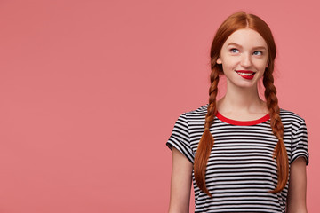Playful chrarming girl with two red haired braids biting red lip within temptation, dressed in...