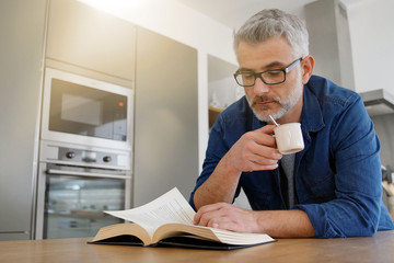 Man reading book at home in modern kitchen