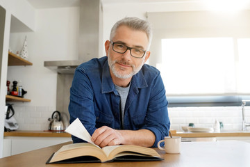 Man reading book at home in modern kitchen
