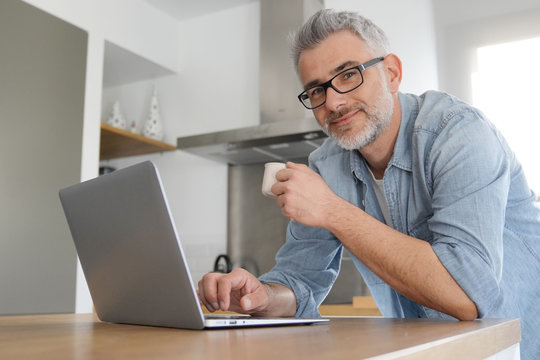 Man With Computer At Home In Modern Kitchen