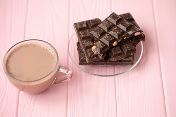 Cup of cocoa and dark chocolate on a pink wooden background