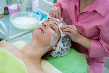 Obraz na płótnie Canvas Natural makeup and beautiful clear skin. Doctor removes the remnants of the cream mask from the skin of the girl in the beauty salon.