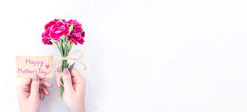 May mothers day idea concept photography - Beautiful blooming carnations tied by rope kraft bow holding in woman's hand isolated on bright modern table, copy space, flat lay, top view