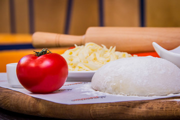 Pizza ingredients on the wooden board - cheese, tomato, sauce, dough