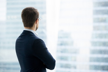 Rear view of businessman in suit standing looking through window