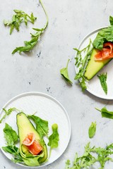 Ripe avocado boats with slices of salted trout, salmon and fresh greens on a gray background. Avocado boats stuffed with salmon with lime, spinach leaves and arugula, concept healthy food, diet.