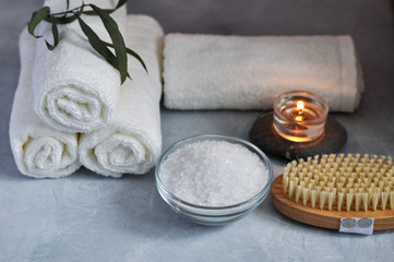 Obraz na płótnie Canvas Close up view of Spa relax concept. White Terry towels, stones, candle, sea salt and wooden massage brush on a gray textured background.