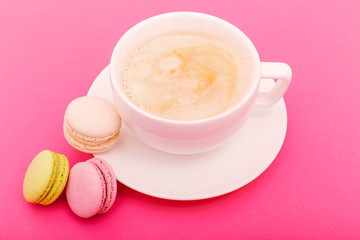 Cozy morning breakfast. Cup of coffee and colorful macaron on pink background top view. Fashion flat lay. Sweet macaroons.