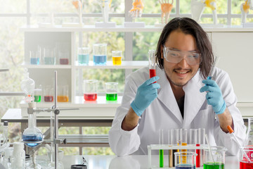 Asian  scientist or chemist  checking test tubes in laboratory, The young man wearing safety glasses in medical experiment. Healthcare, pharmaceutical research and development concept with copy space.