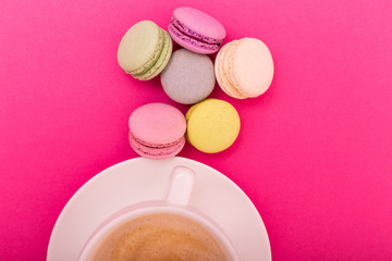 Obraz na płótnie Canvas Cup of coffee with color macaron on pink background from above, flat lay