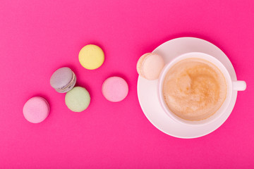 Cup of coffee with color macaron on pink background from above, flat lay