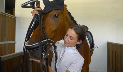 CLOSE UP: Young woman tacking up and putting a bridle on her beautiful horse.