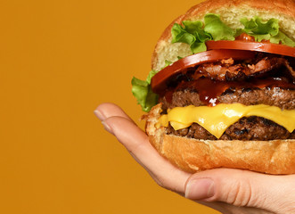 Close up photo of big cheeseburger burger sandwich with beef bacon cheese and tomatoes on yellow