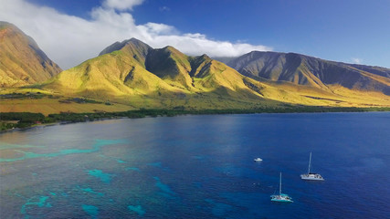 Aerial view of the west coast of Maui with visible coral reef, sailing boats and green mountain on...