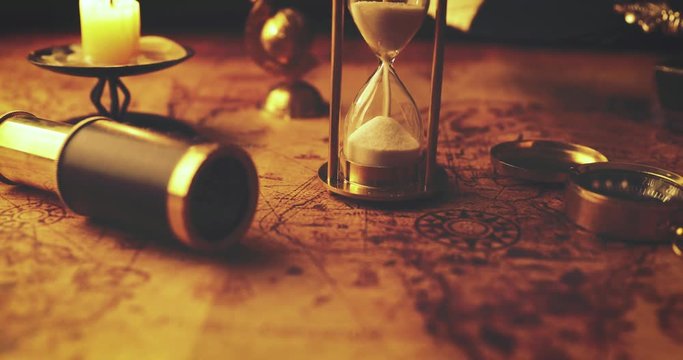 closeup of sandglass running out on old world map in candlelight