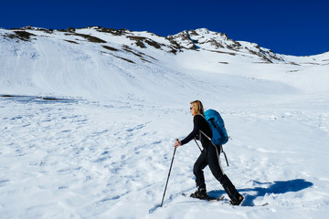 Fototapeta na wymiar A sporty woman wirh blond hair is walking with snoweshoes the a summit in the alps of italy