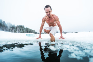 Young man with lean muscular body going to swim in the cold winter water with ice floating on the...