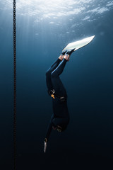 Freediver in monofin descends into depth along the anchor chain in the sea