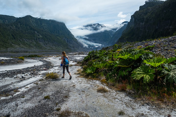 Fototapeta na wymiar Woman hiker walks in the valley in the wild area with lush vegetation and glacier on the horizon
