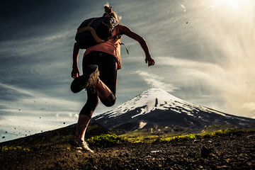 Young woman, trail running athlete runs on the trail with loose ground and volcano on the background