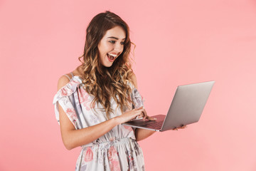 Photo of brunette woman 20s in dress holding and using silver laptop