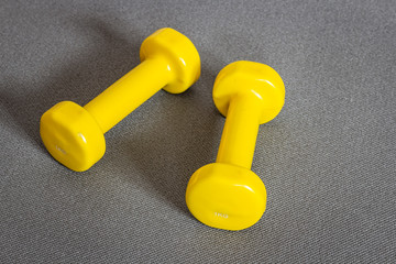 Yellow dumbbells on grey fitness mat. Concept of fitness and weight loss.