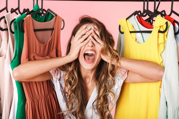 Photo of joyful woman in dress standing inside wardrobe rack full of clothes