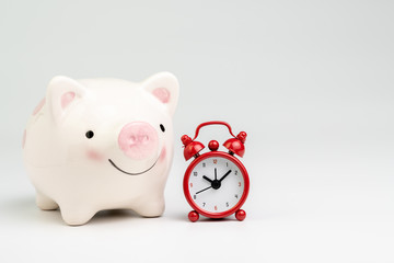 Time is money or long term savings and investment concept, smile pink piggy bank with red alarm clock on white background with copy space