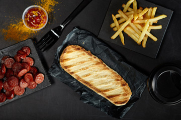 Grilled bun, sausages, french fries and cup of coffee to go on black background